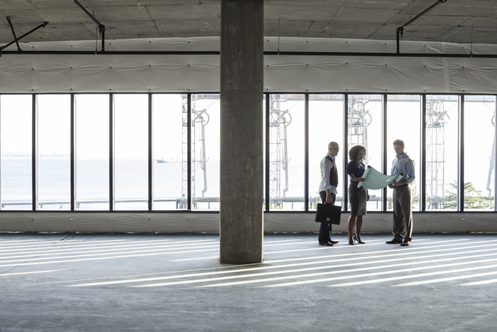 Three people reviewing blueprints in empty office